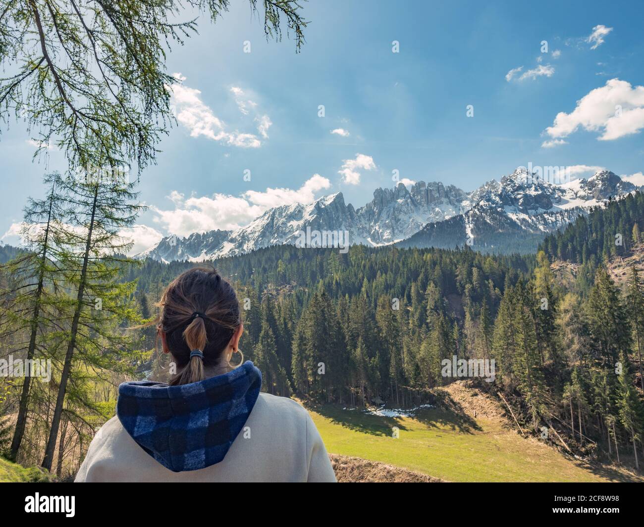Back view of young Woman in sweater protecting face from sun by hand and  looking at majestic landscape of rocky mountains and forest in cloudy day  Stock Photo - Alamy