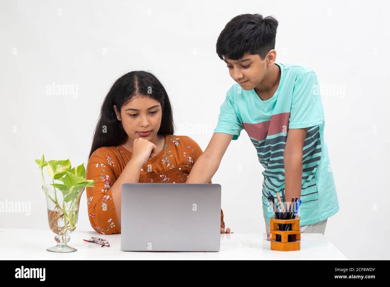 A boy points to a laptop as the girl sits on a table, distance learning for students, study from home, online education, Discussing project. Stock Photo