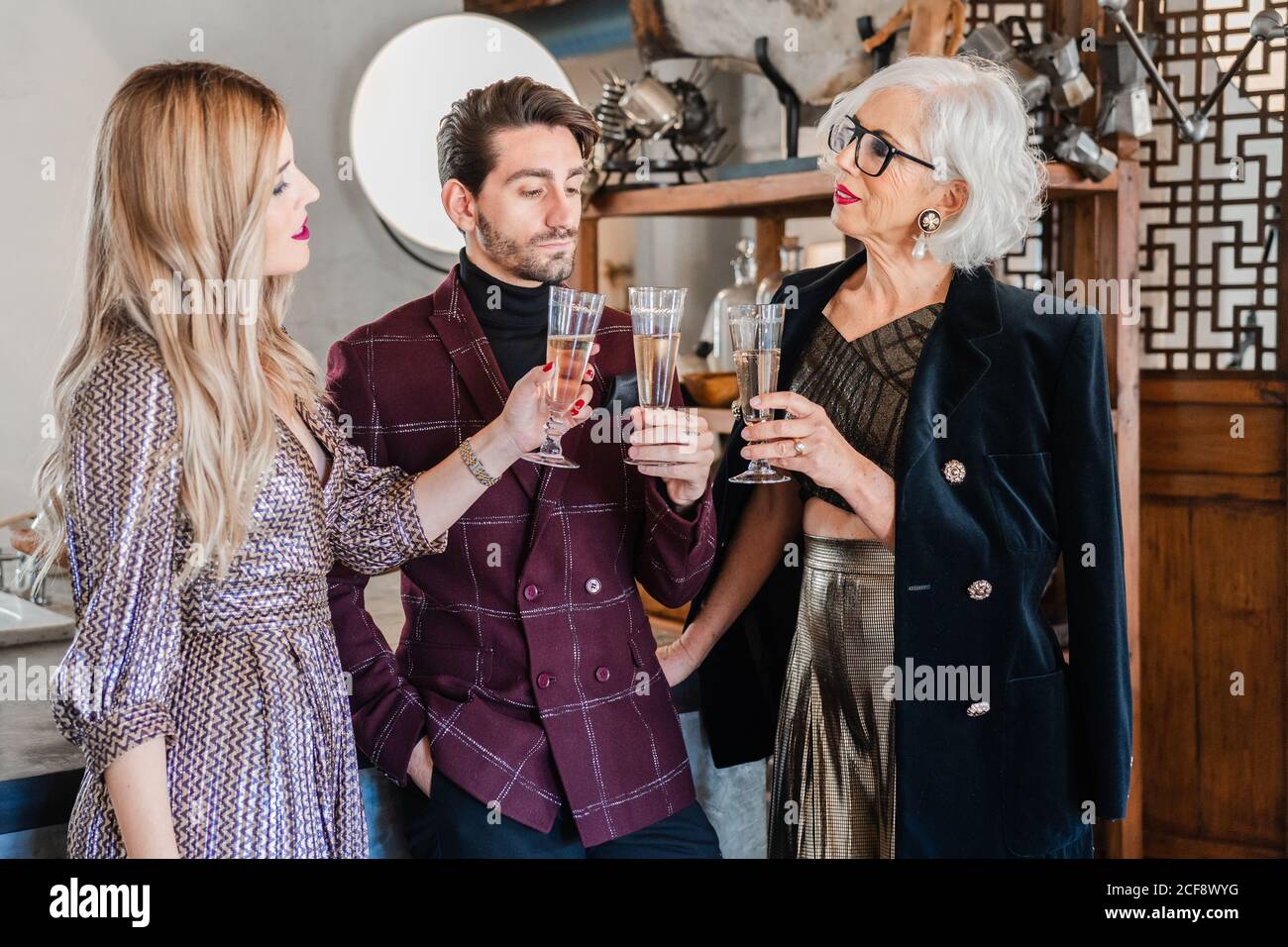 Pensive senior Woman in stylish clothes and adult children congratulating each other with family event while drinking champagne together at home Stock Photo