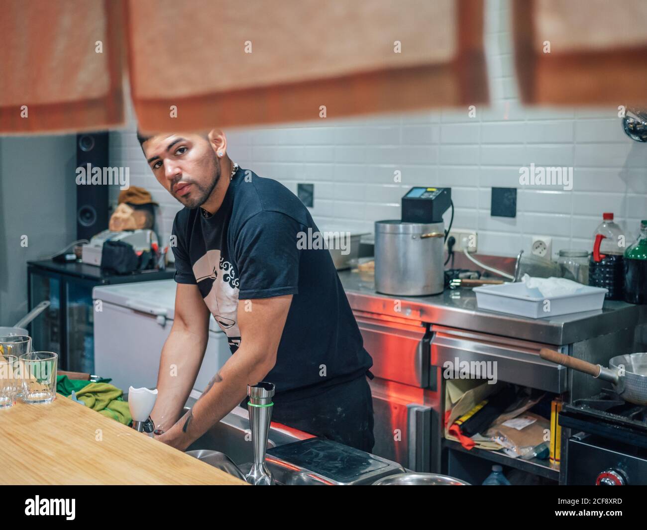 Handsome ethnic young man washing hands while working in Japanese restaurant and cooking ramen Stock Photo