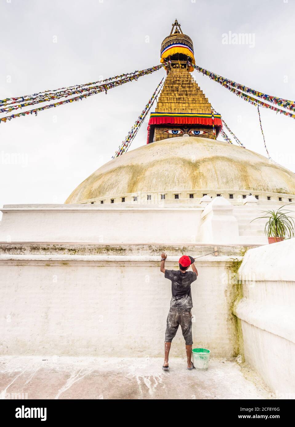 NEPAL, BOUDHANATH STUPA - AUGUST 19, 2014: Back view of young worker painting stone wall with lime wash Stock Photo