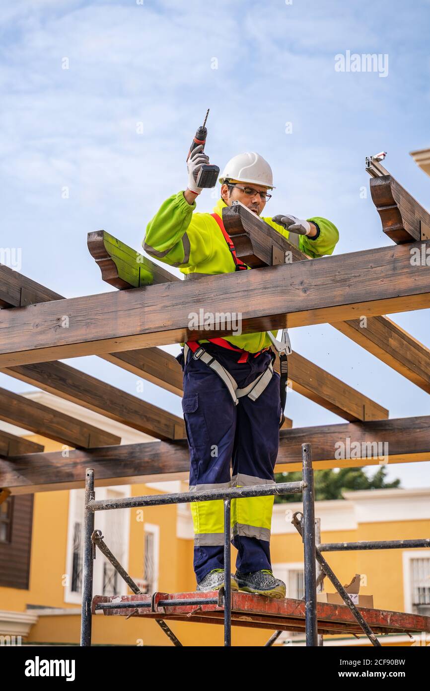 From below of male technician in work wear standing on scaffolding and preparing for installation of solar panel on wooden construction Stock Photo