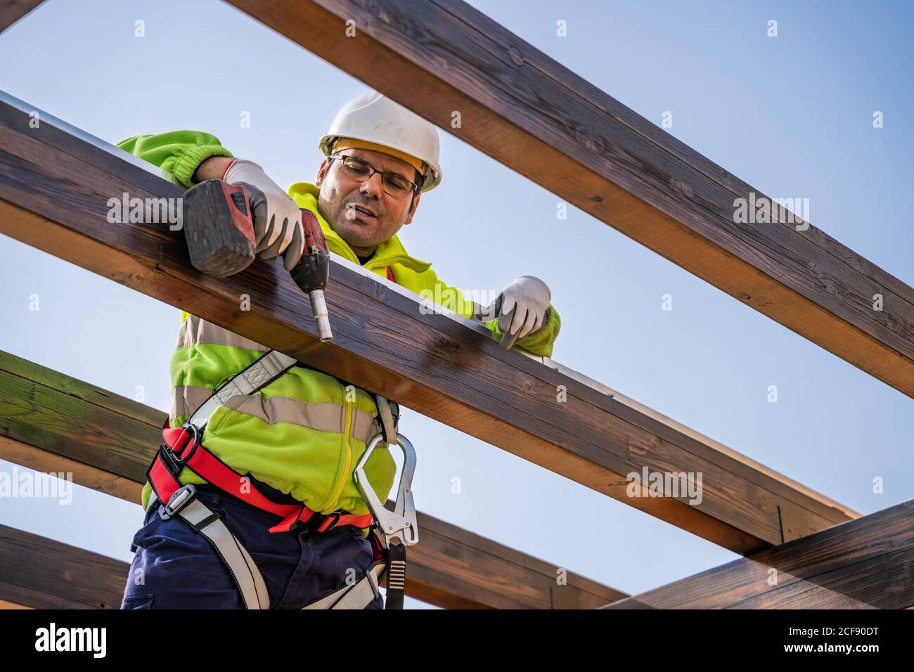 From below of male technician in work wear standing on scaffolding and preparing for installation of solar panel on wooden construction Stock Photo