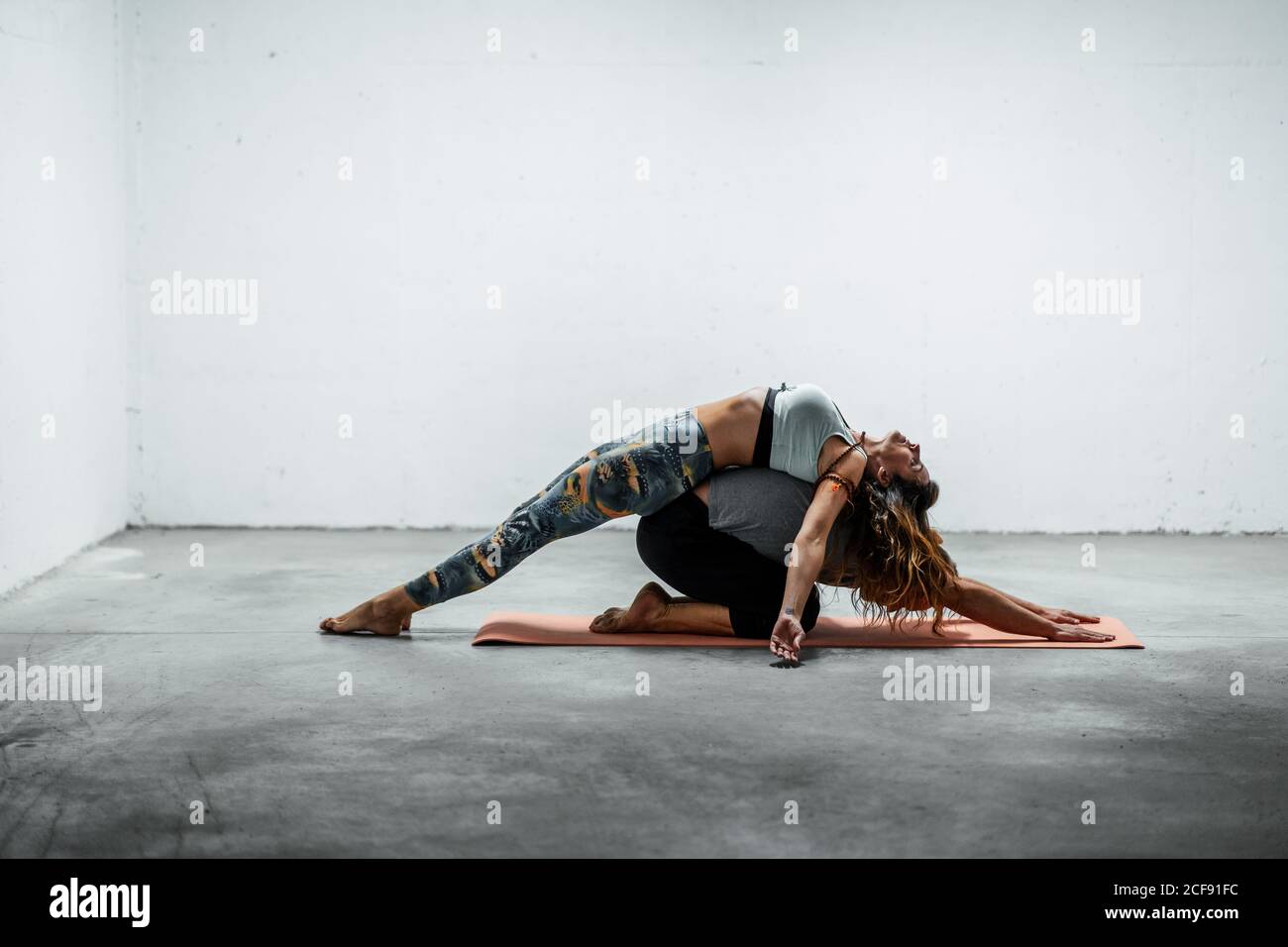 Side view of flexible man in Child pose and slim Woman in Fish pose on back of partner lying on mat Stock Photo
