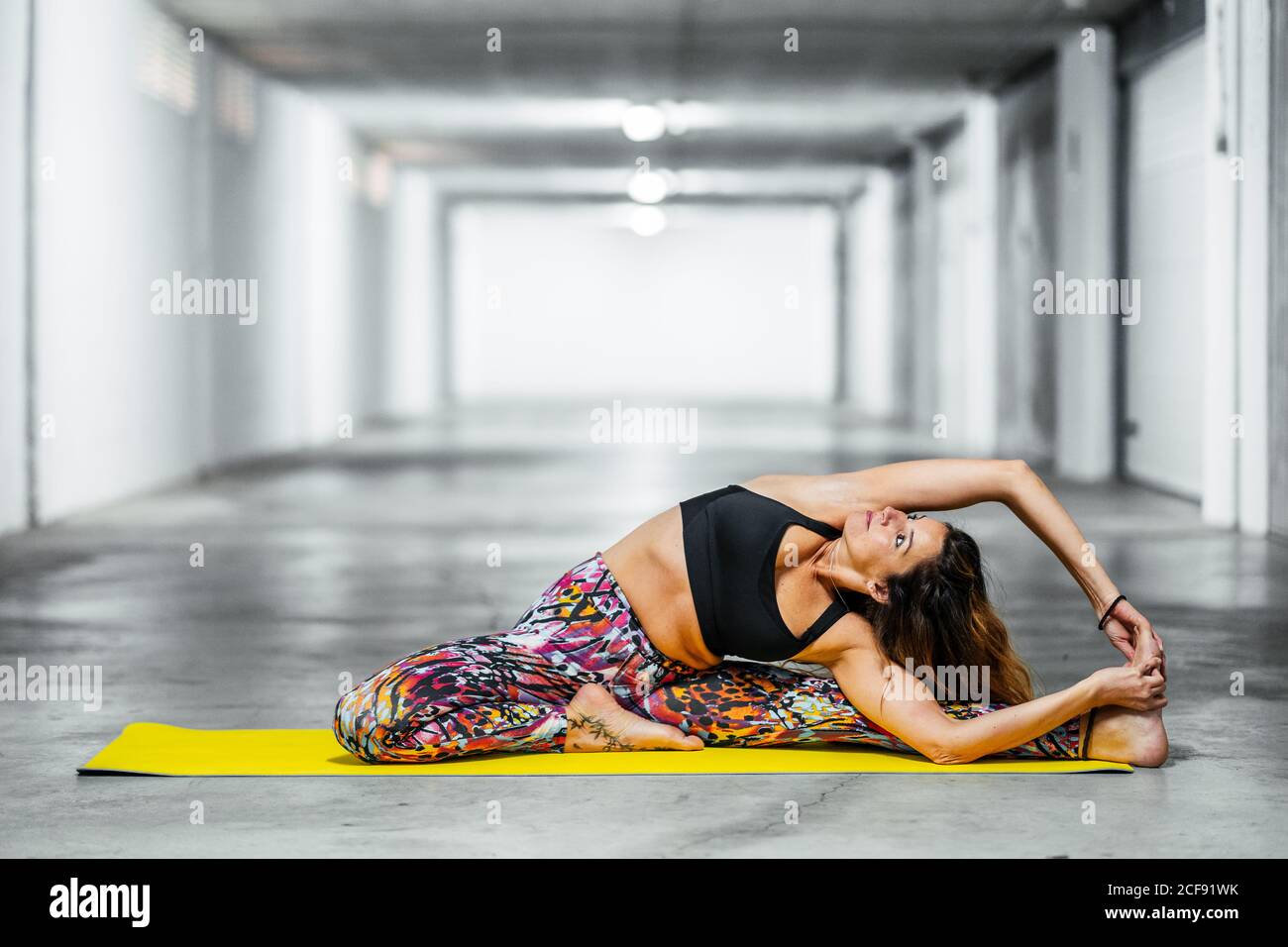 Side view of adult Woman in revolved head to knee pose while practicing yoga in light garage hall looking up Stock Photo