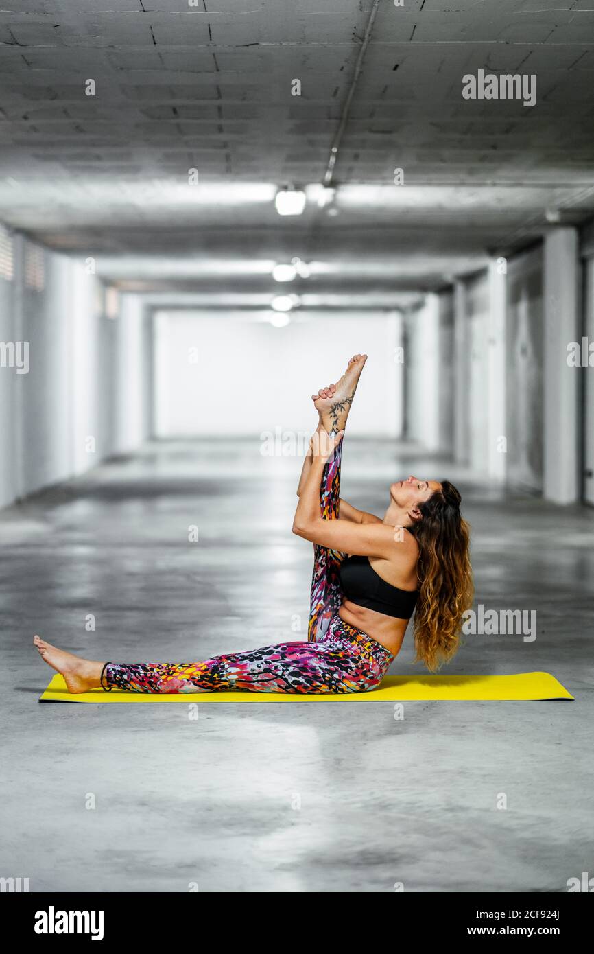 Side view of fit female in active wear performing modified Heron pose with extended leg while practicing yoga in spacious light hall Stock Photo