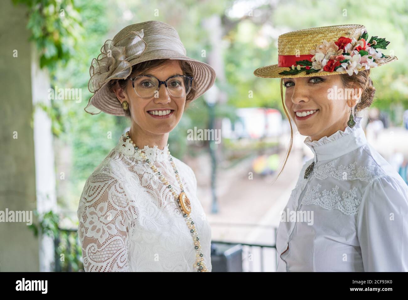 Women in retro hats and blouses smiling and looking at camera while standing on blurred background of park Stock Photo