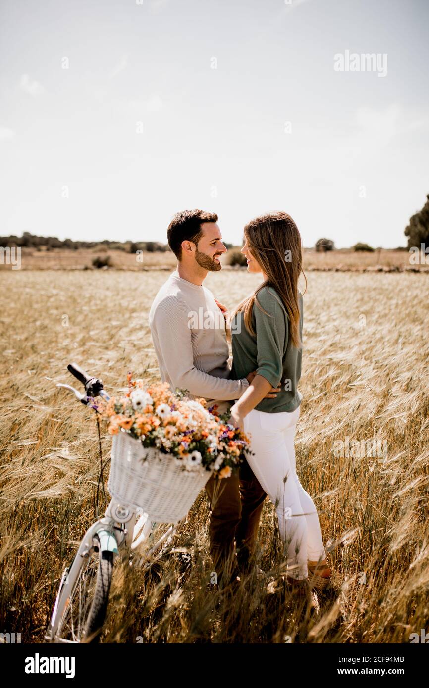 Side view of amorous couple posturing near vintage bike on wheat field in summertime Stock Photo