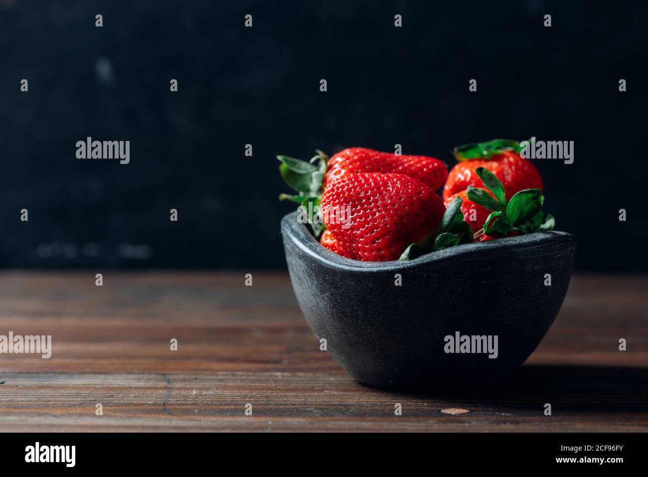 Fresh ripe strawberries in black concrete bowl on wood background Stock Photo