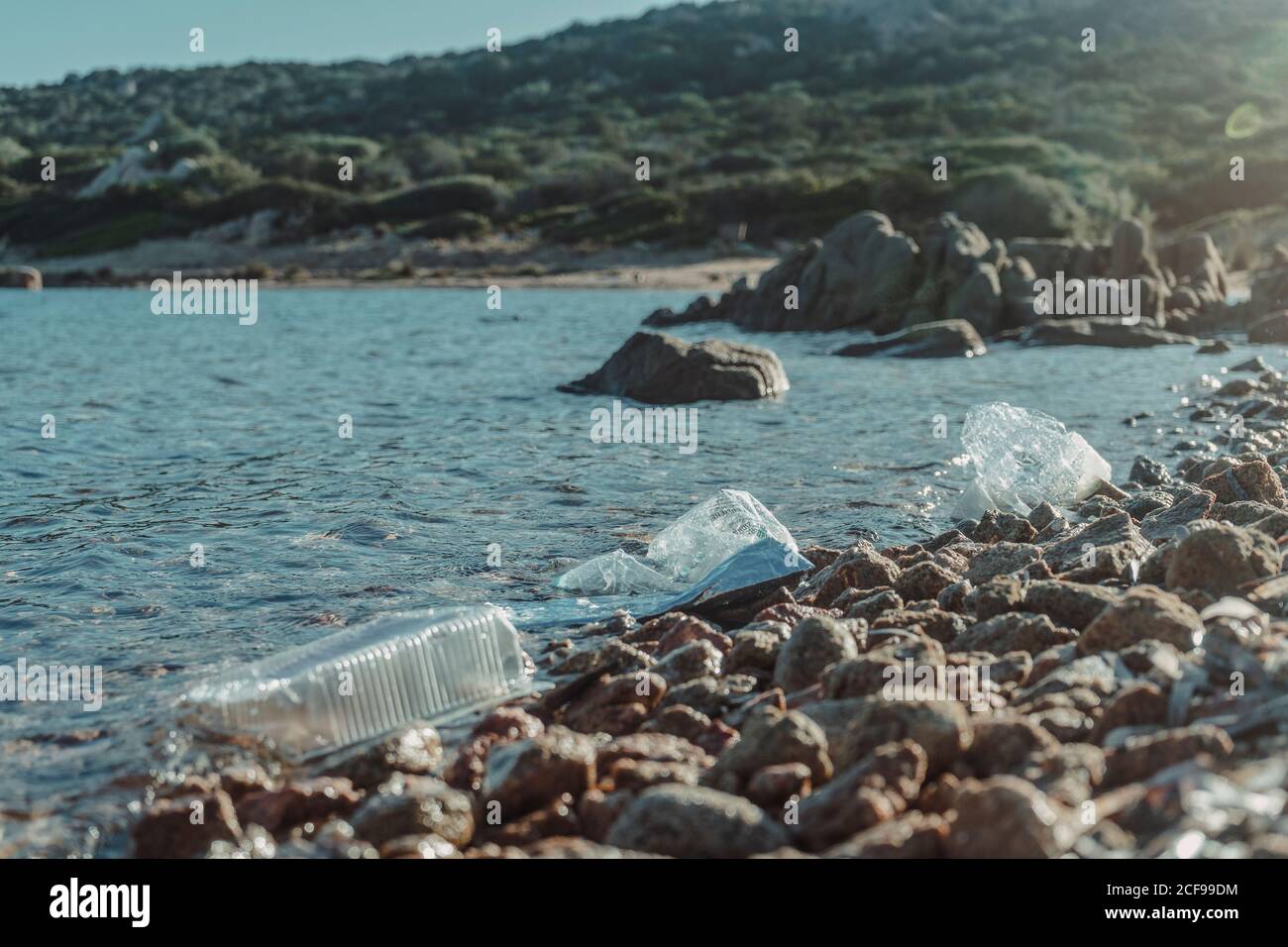 Empty plastic crumpled bottles waste lying on the seaside rock near clear water Stock Photo