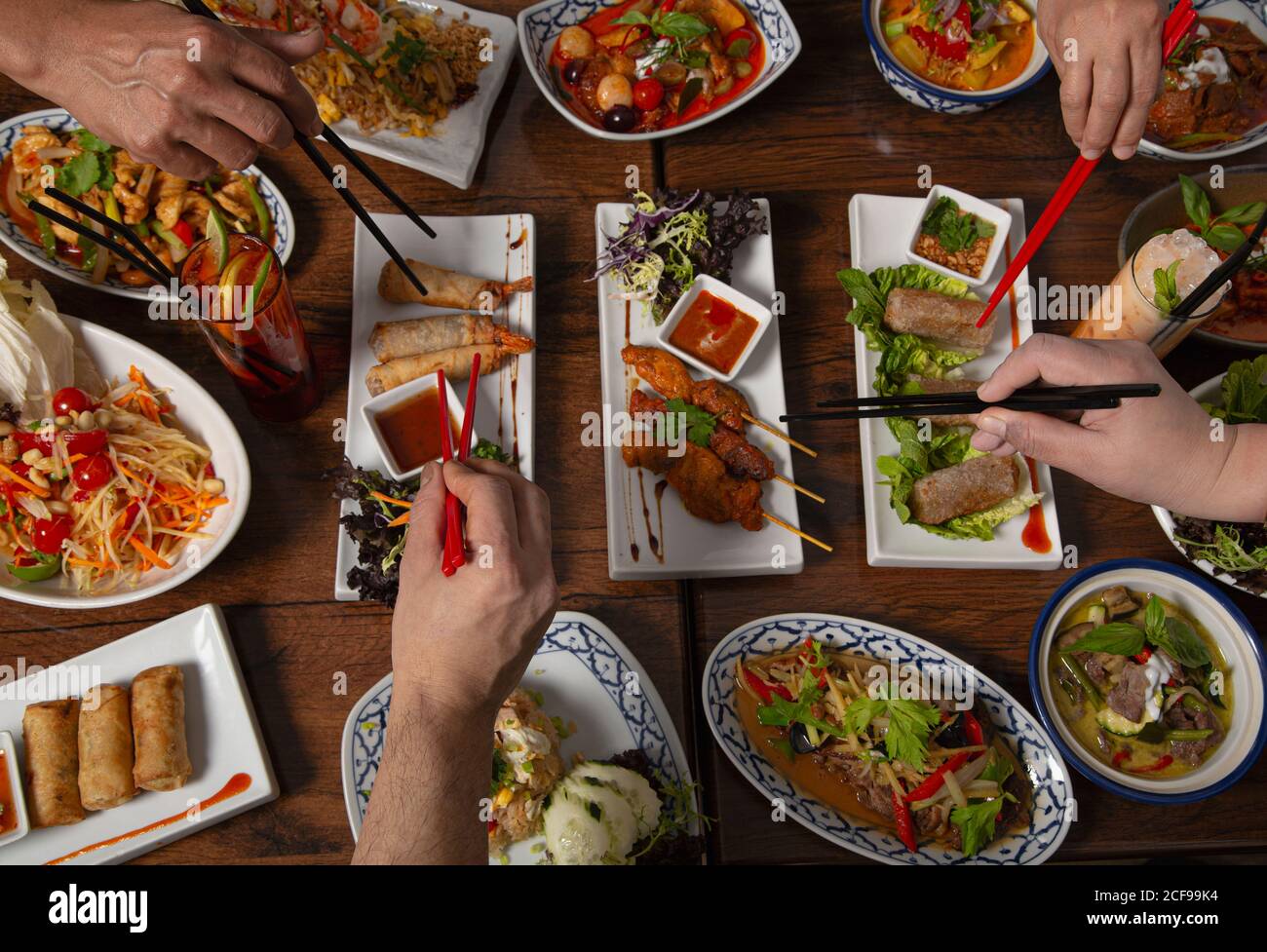 From above cropped unrecognizable people with chopstick eating assorted colorful spicy Thai food served for family dinner on wooden table Stock Photo