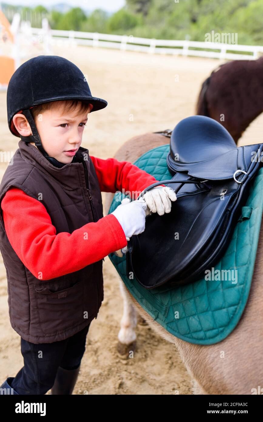 Side view of little jockey in protective helmet adjusting stirrup on