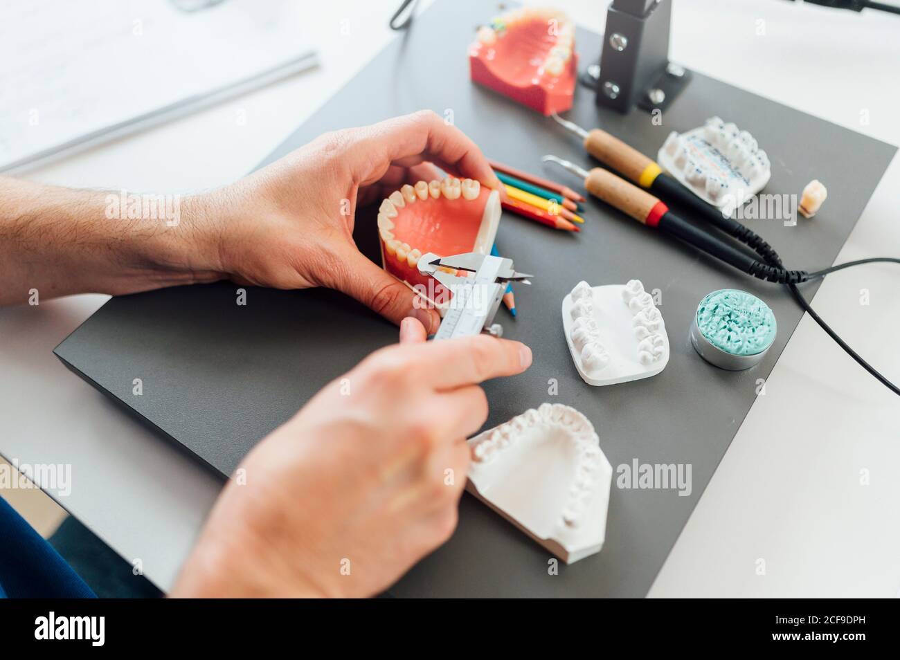 From above of crop male dentistry student using caliper for measuring dental prosthesis while working at table with tools during class Stock Photo