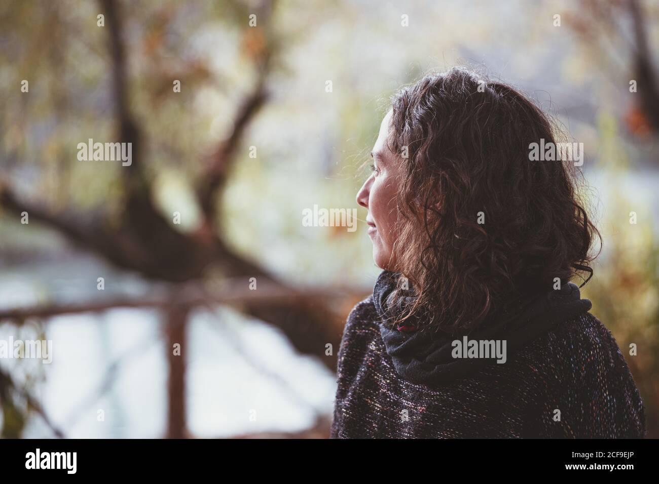 Adult lady with curly hair looking away and thinking while standing on blurred background of peaceful autumn park Stock Photo