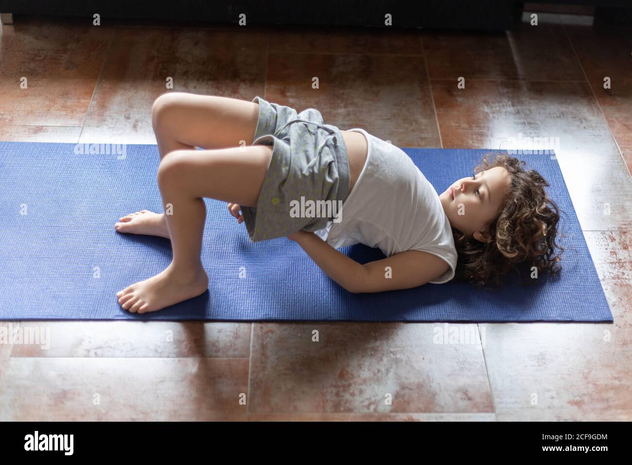 From above side view of little girl in casual sportswear performing Bridge  pose on mat while practicing yoga at home Stock Photo - Alamy