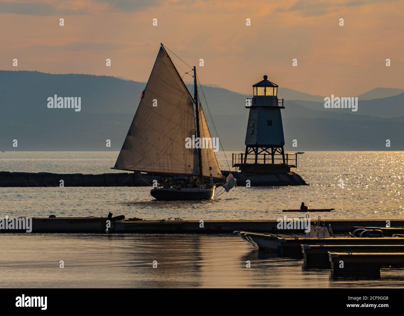 a sloop sailing by the lighthouse on the waterfront of Lake Champlain in Burlington, Vermont Stock Photo