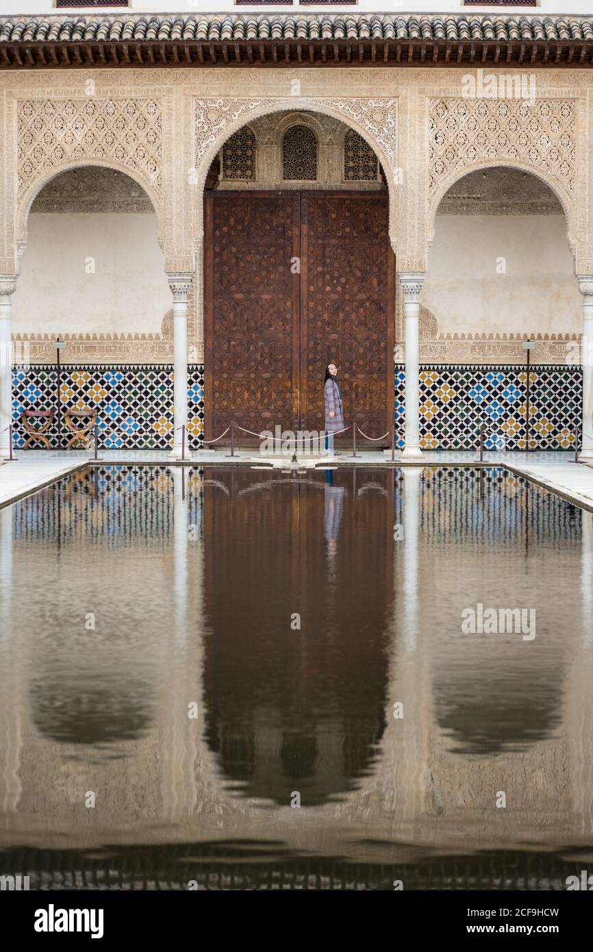 Distant female standing near calm pool and ornamental door outside ancient Islamic palace Stock Photo