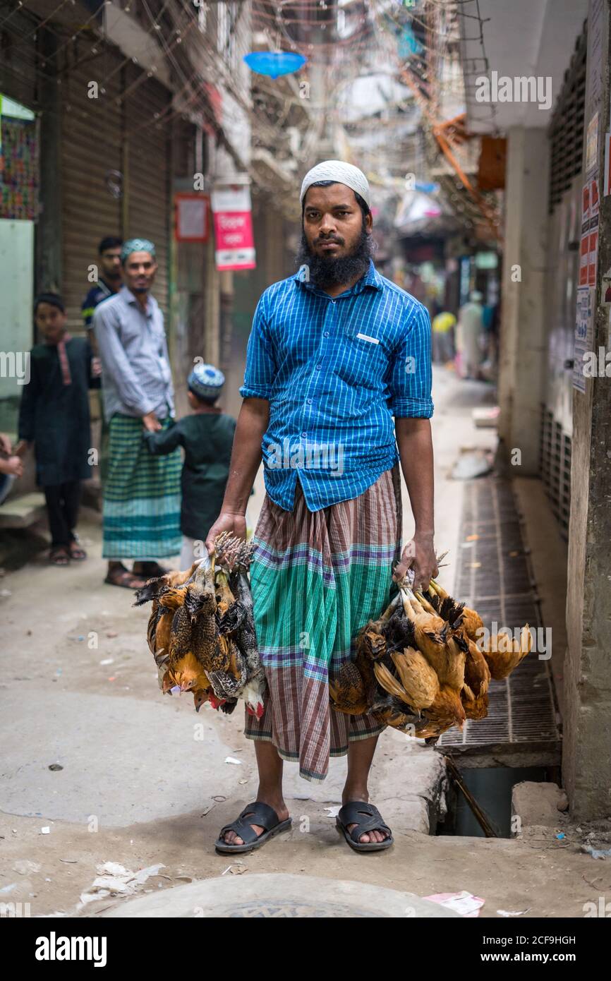 Bangladesh - January, 25 2019: Bearded ethnic man with bunches of dead chickens standing on shabby street in city Stock Photo