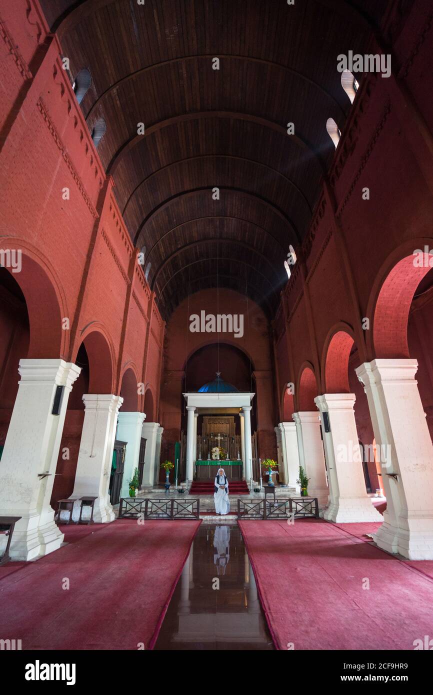 From below interior of roof and entrance with arches and nun standing at altar in Barisal in Bangladesh Stock Photo