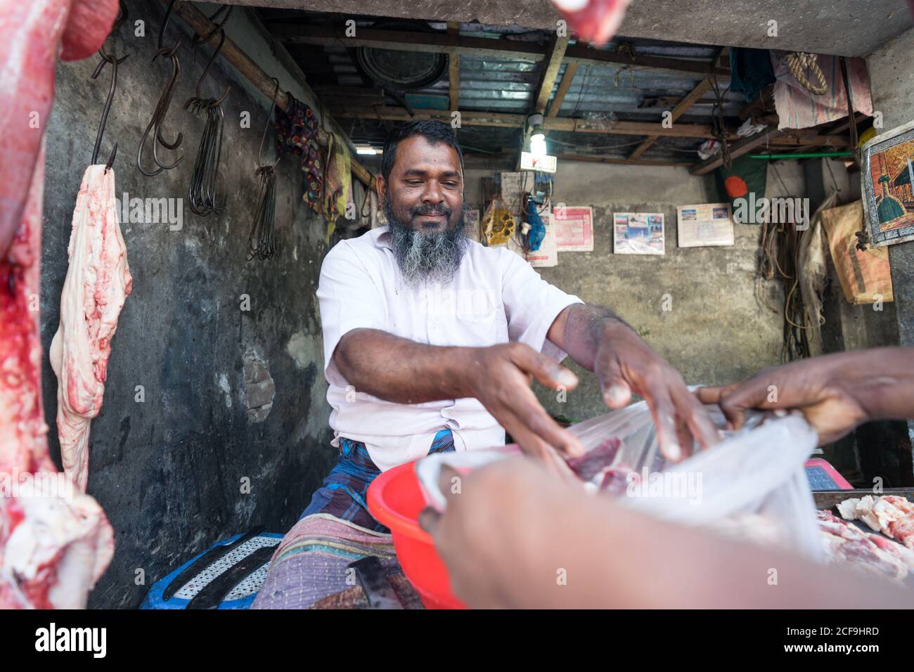 Satisfied matured ethnic bearded male butchery owner packing meat in plastic bag for customer in Barisal in Bangladesh Stock Photo