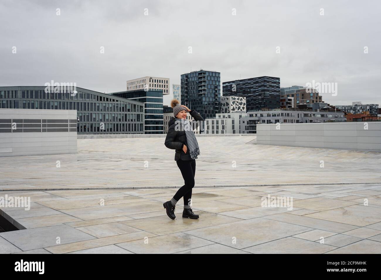 Cheerful young ethnic Woman wearing winter clothes and standing on plaza at  Oslo Opera House Stock Photo - Alamy