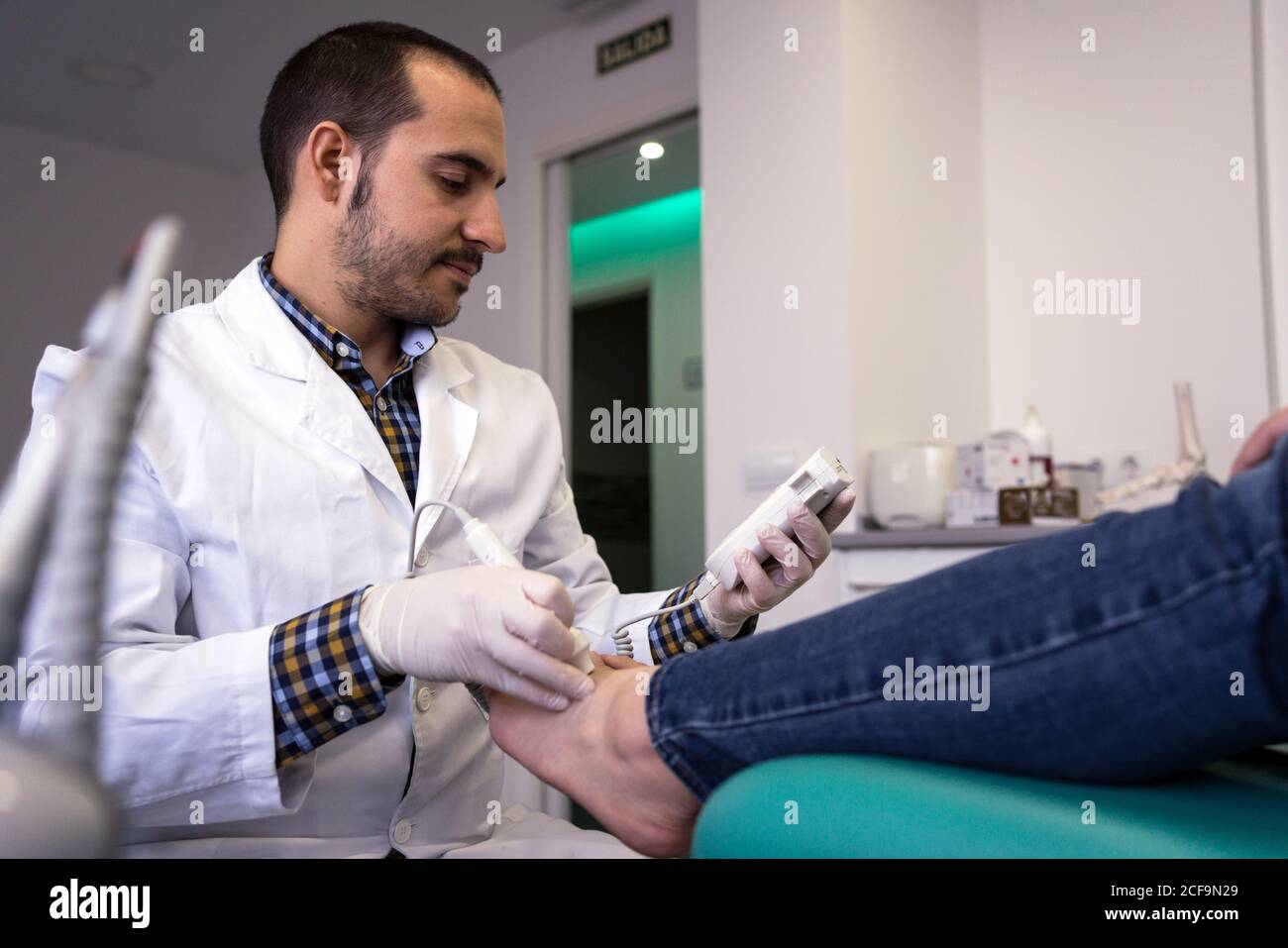 Male podiatry doctor in white coat using professional equipment while