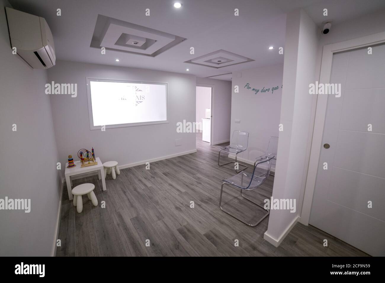 Light waiting room in clinic with laminate floor and transparent chairs and kids area equipped with large display and air conditioner on wall Stock Photo