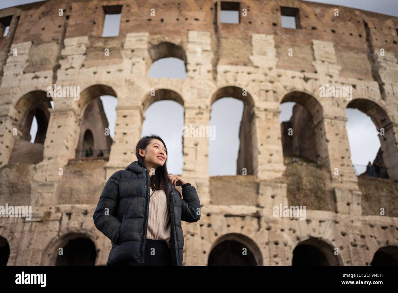 From bellow happy ethnic Woman smiling and looking away while standing on  blurred background of Colosseum on street of Rome, Italy Stock Photo - Alamy, image size:1300x956