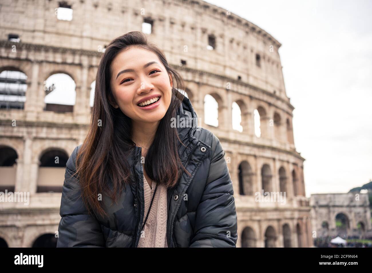 From bellow happy ethnic Woman smiling and looking away while standing on  blurred background of Colosseum on street of Rome, Italy Stock Photo - Alamy, image size:1300x956