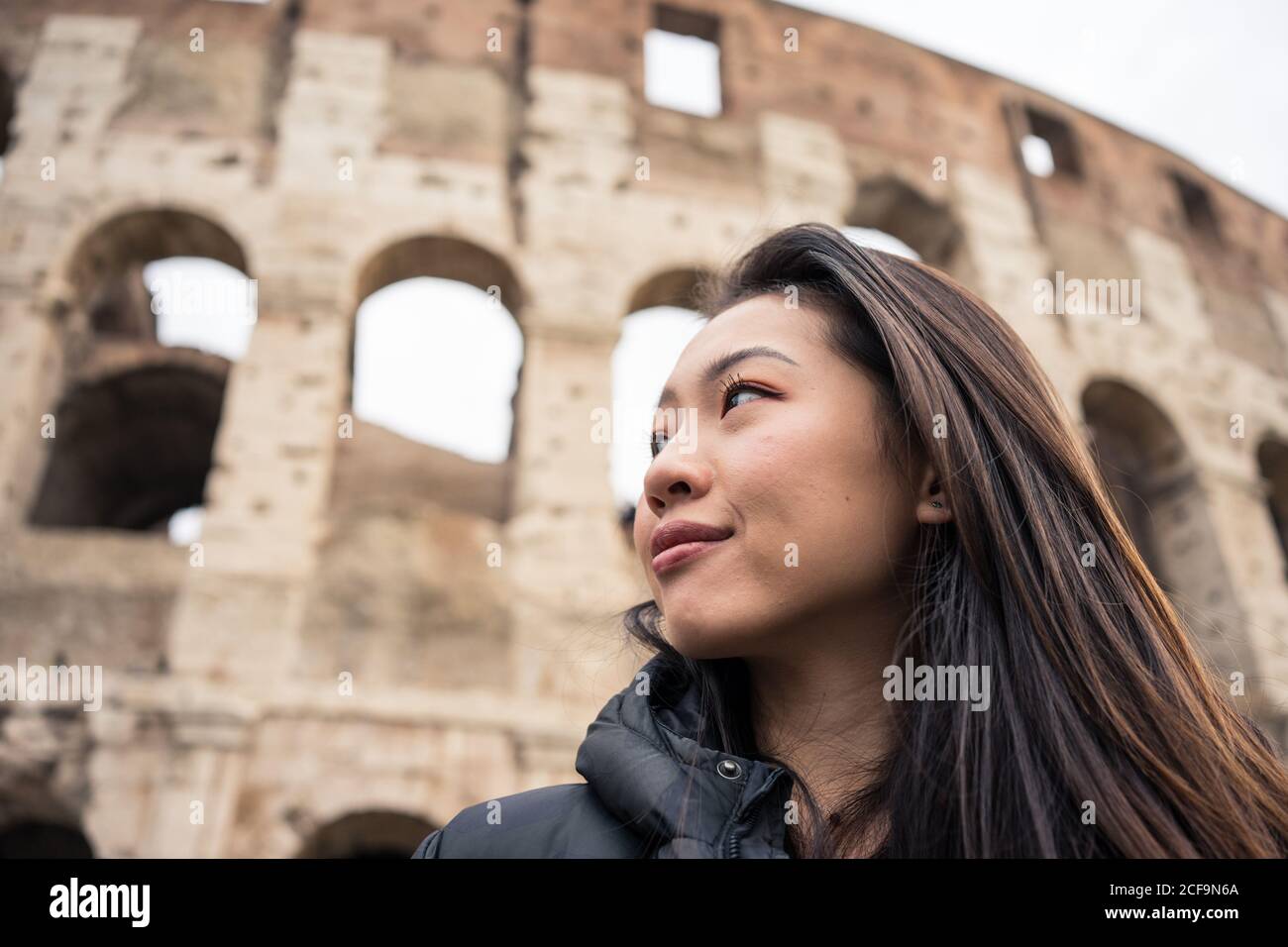 From bellow happy ethnic Woman smiling and looking away while standing on  blurred background of Colosseum on street of Rome, Italy Stock Photo - Alamy, image size:1300x956