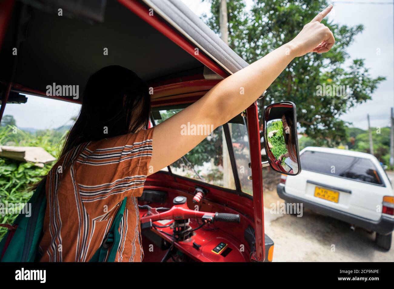 Back view of faceless black haired female traveler in casual wear signalizing with hand while riding in red traditional auto rickshaw at Sri Lanka Stock Photo