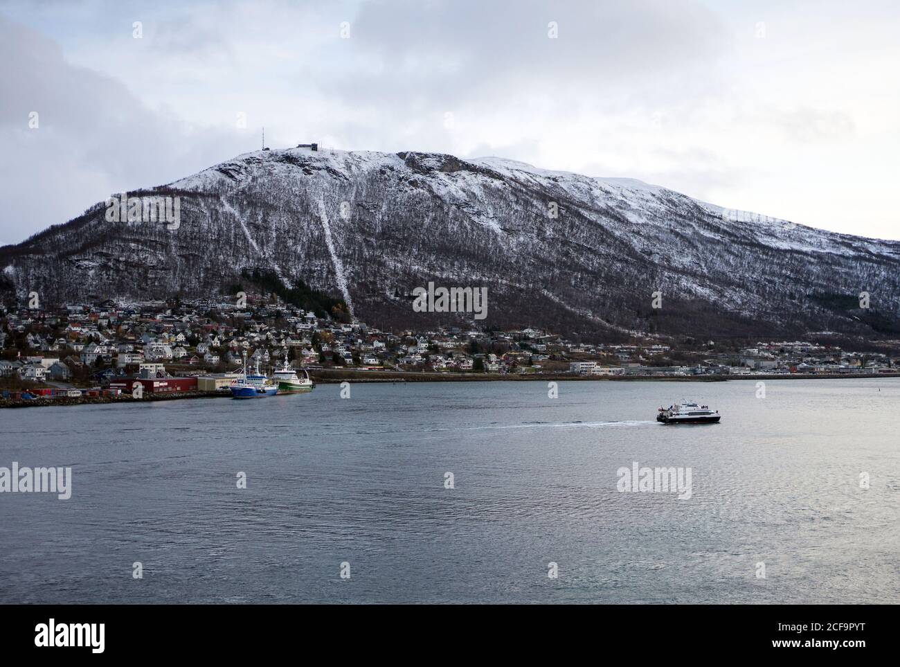 From above of calm bay with city on coast neat powerful snowy mountain with cloudy sky on background at Tromso in Norway Stock Photo