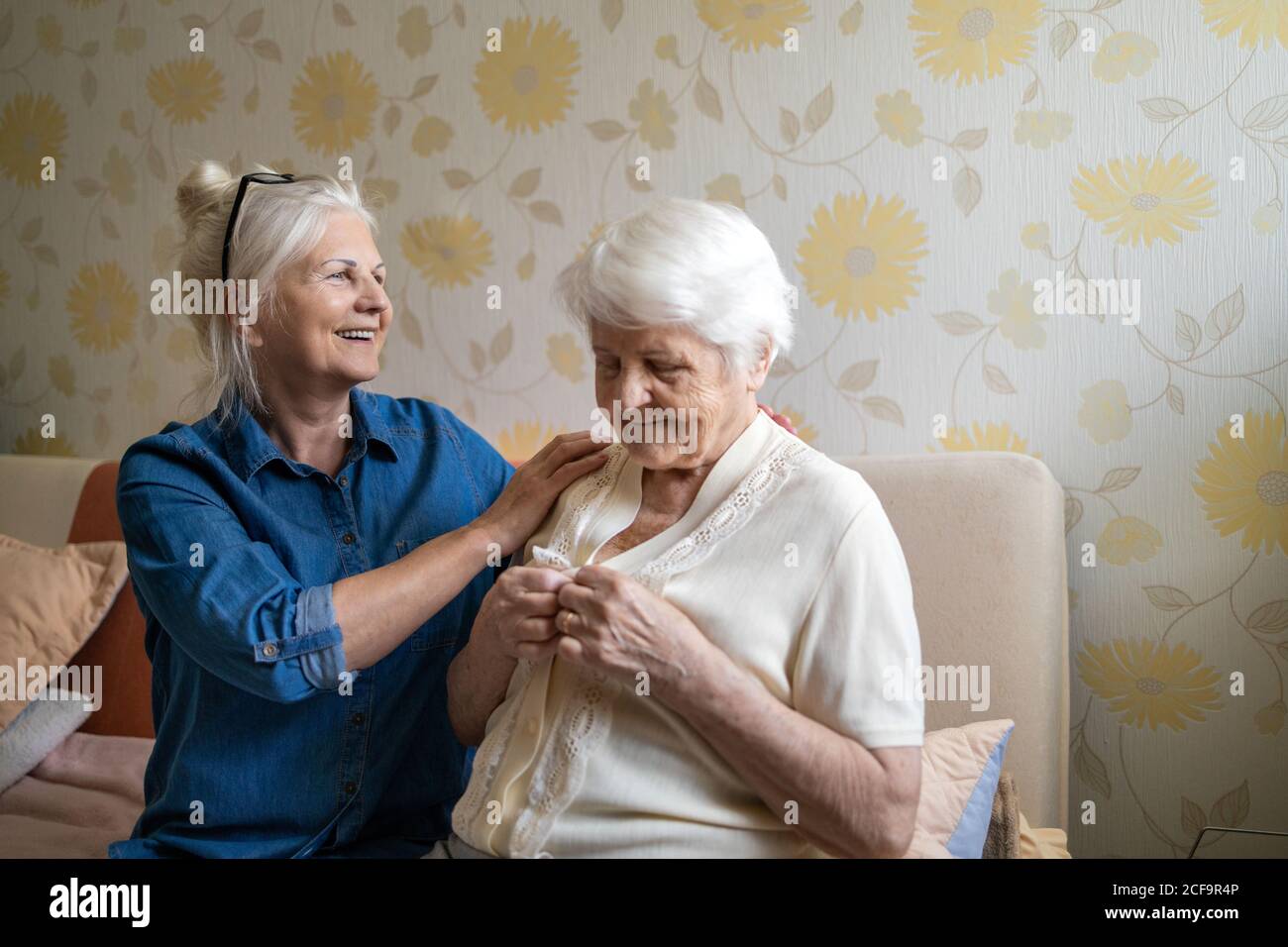 Woman helping senior woman dress in her bedroom Stock Photo