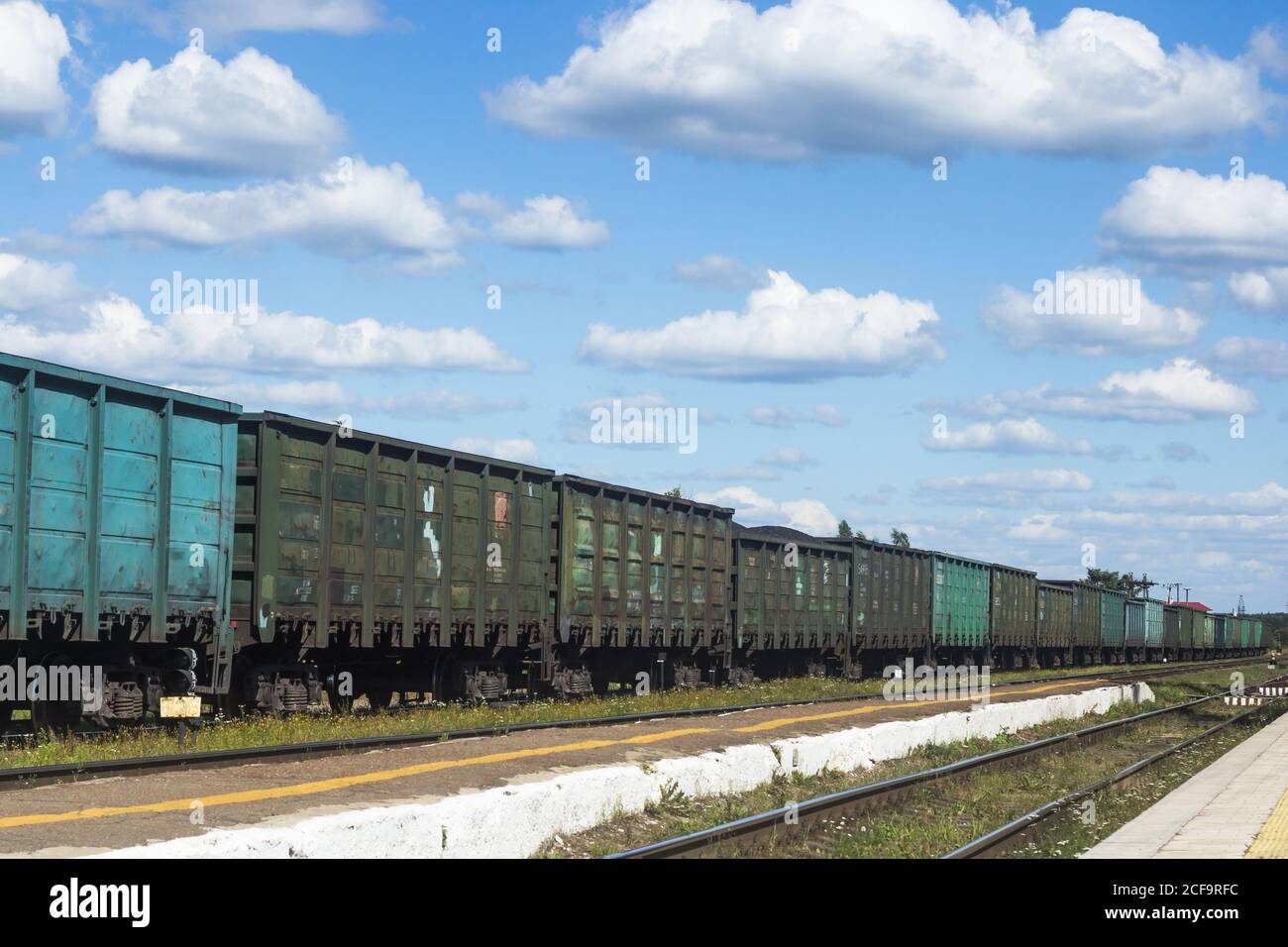 a freight train stands on the railway tracks against a background of blue sky and clouds Stock Photo