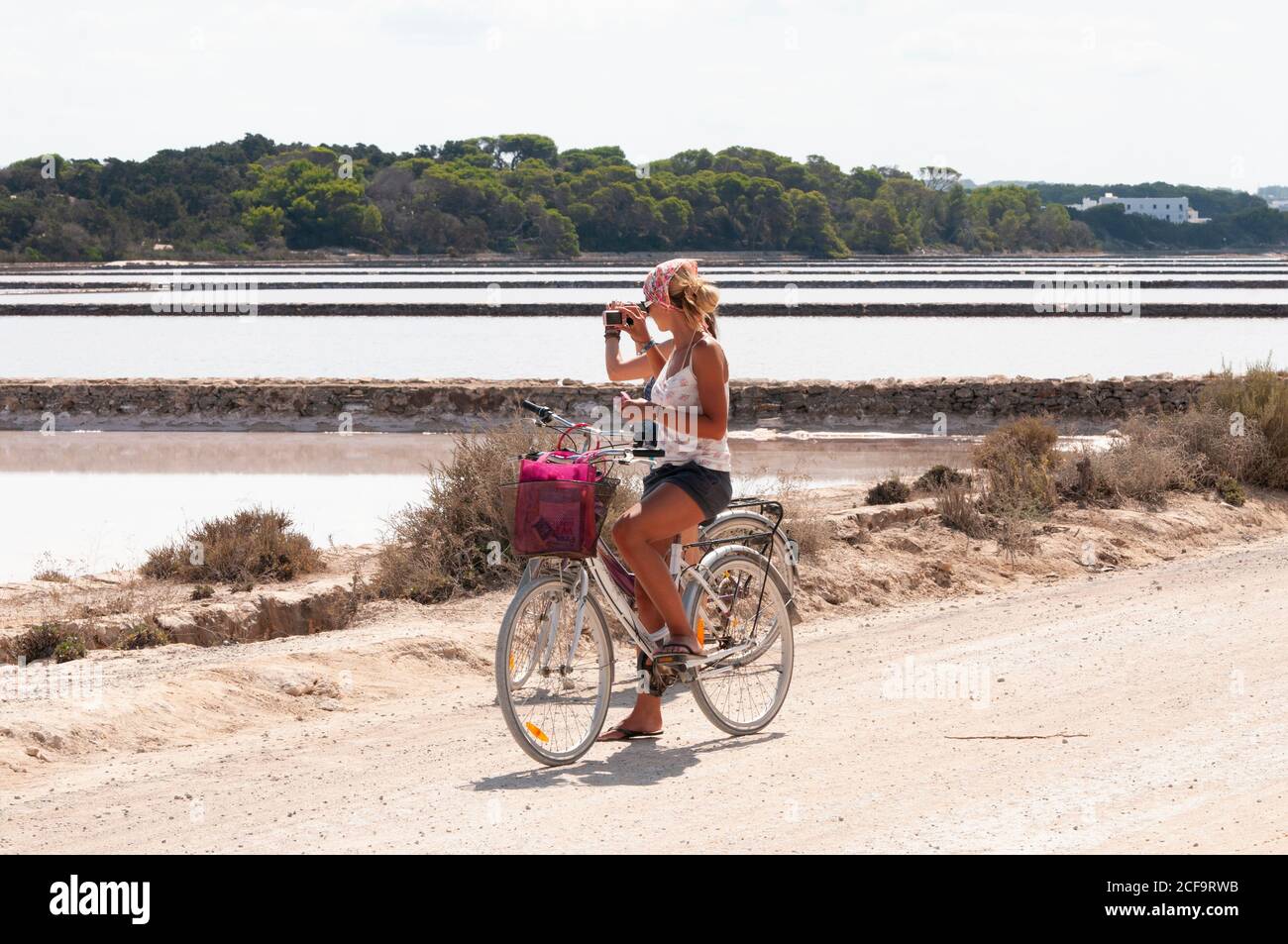 Two beautiful girls on bicycles ride the salt flats of the island of Formentera, Spain, Mediterranean island. Girl photographs the island landscape wi Stock Photo