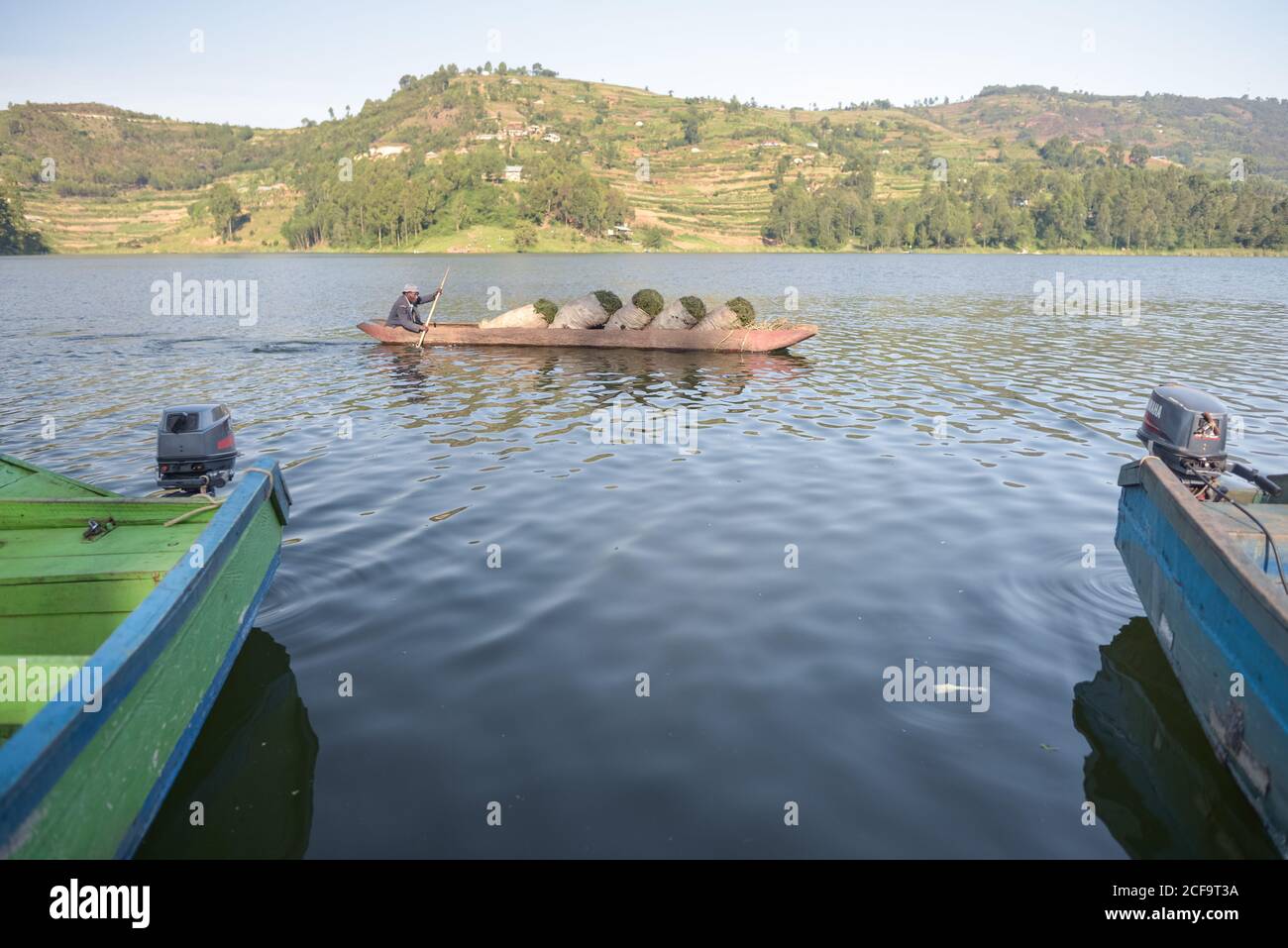 Uganda - November 26, 2016: Adult African man in a wooden boat with sacks of fresh green tea leaves arriving to a pier to trade among others on rural market Stock Photo