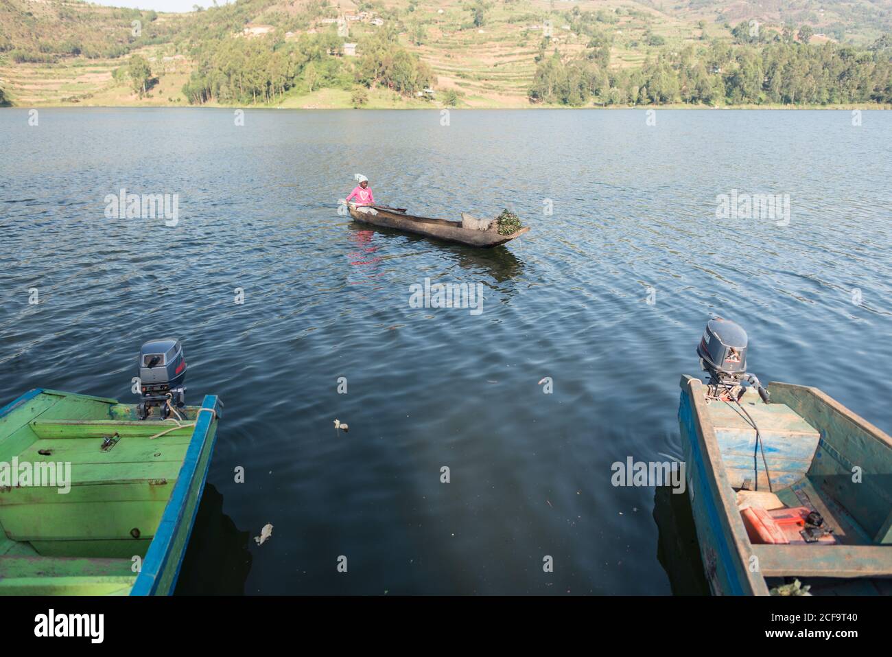 Uganda - November 26, 2016: Adult African man in a wooden boat with sacks of fresh green tea leaves arriving to a pier to trade among others on rural market Stock Photo