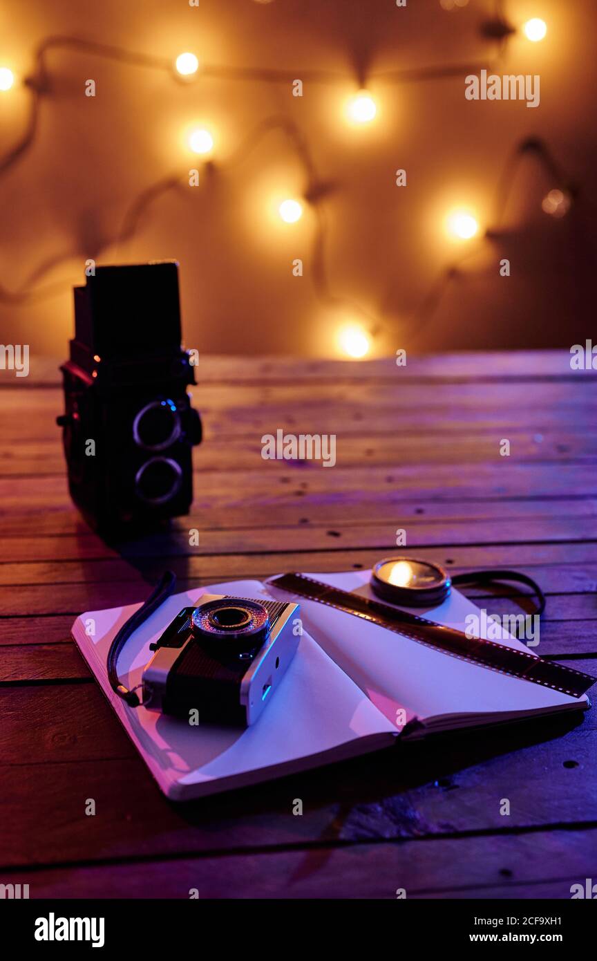Black retro photo camera with notebook and film composed with vintage radio on wooden table in garland light Stock Photo
