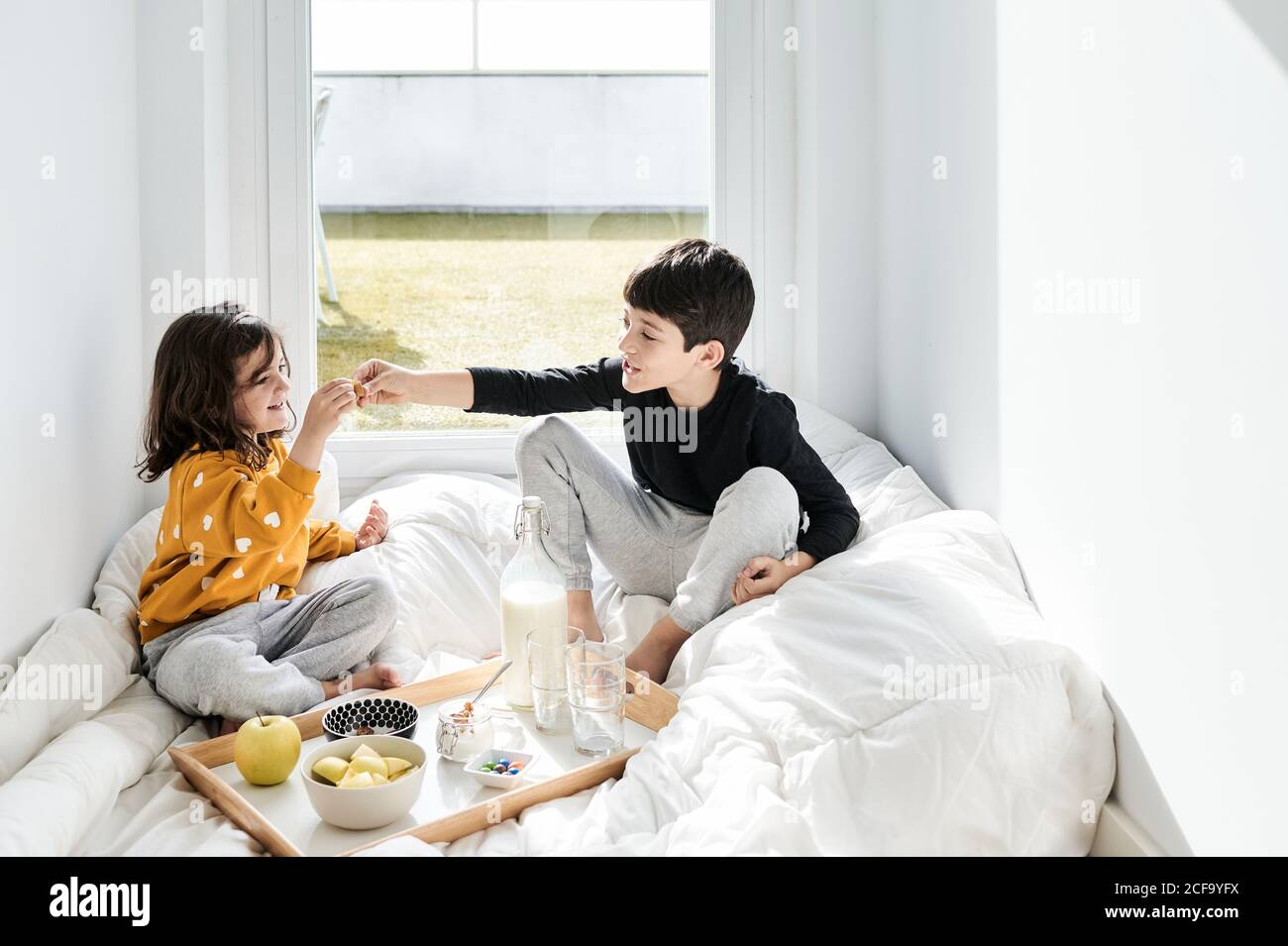 Smiling brother and sister in casual clothes sitting on soft white