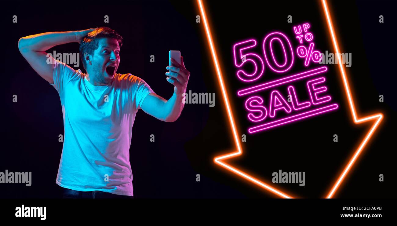 Selfie, astonished. Portrait of young man in neon on dark studio backgound. Human emotions, black friday, cyber monday, purchases, sales, finance concept. Copyspace. Seamless post for instagram. Stock Photo
