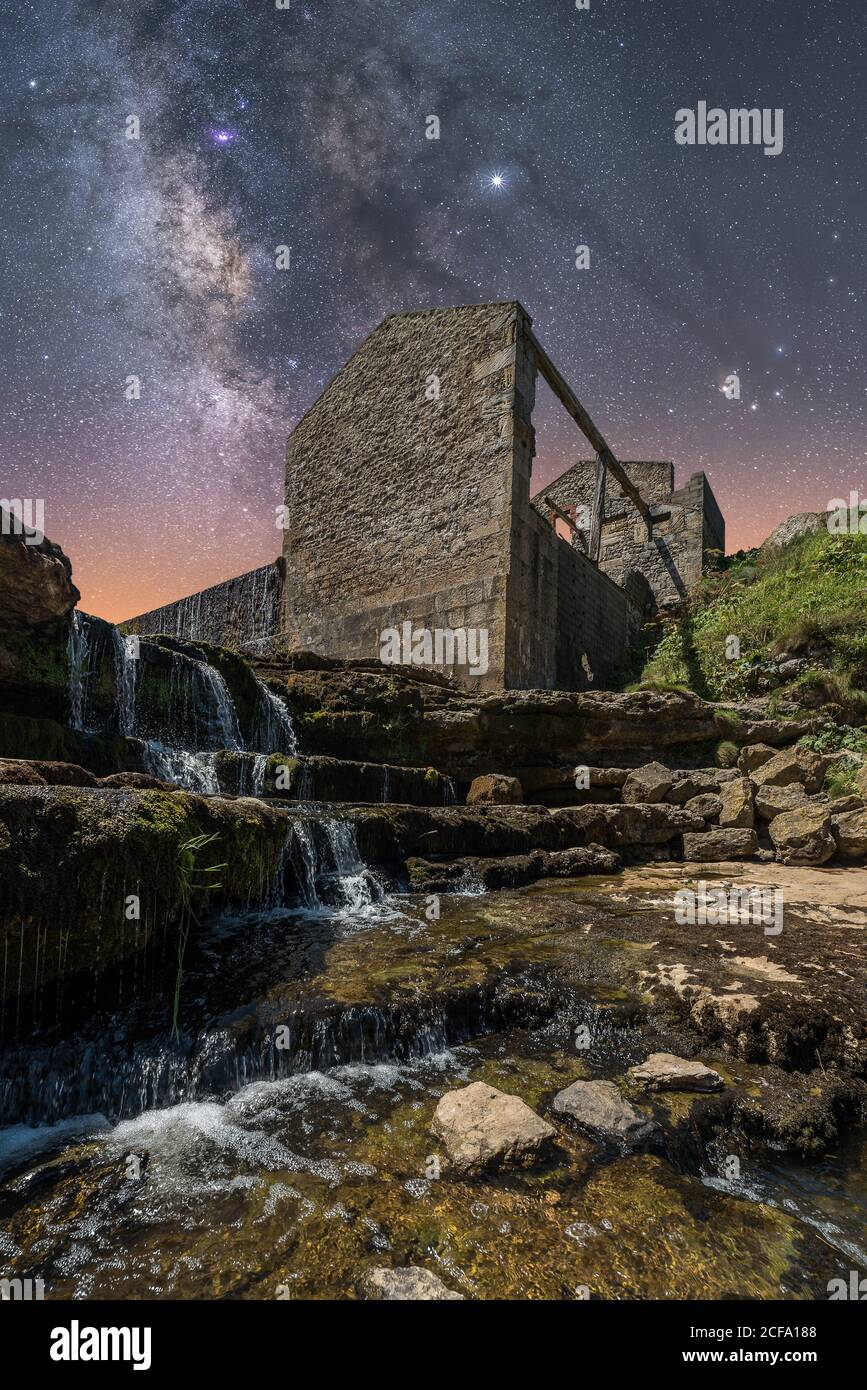 From below of ancient stone castle and small waterfall on stairs under dark sky with stars and milky way Stock Photo