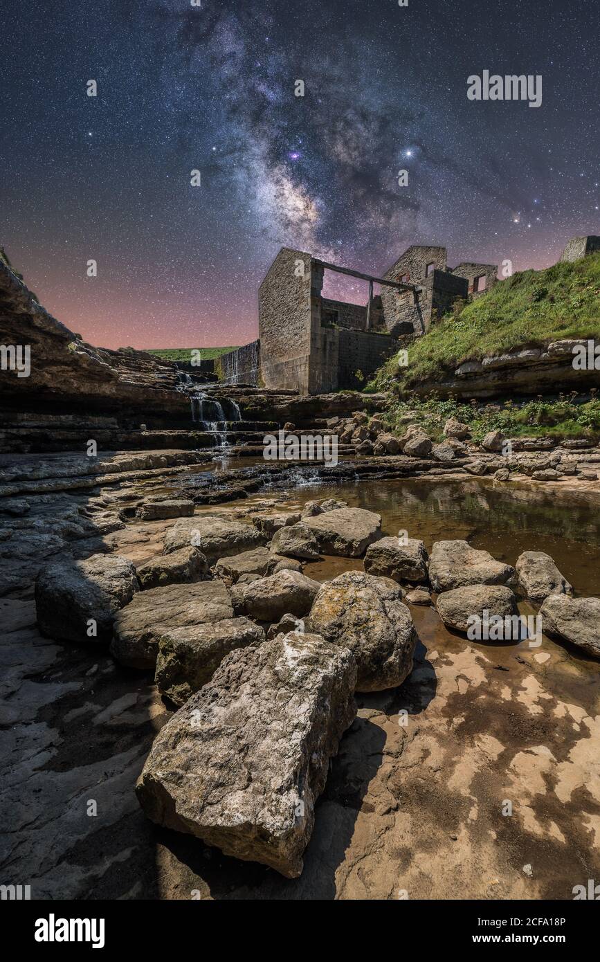 From below of ancient stone castle and small waterfall on stairs under dark sky with stars and milky way Stock Photo
