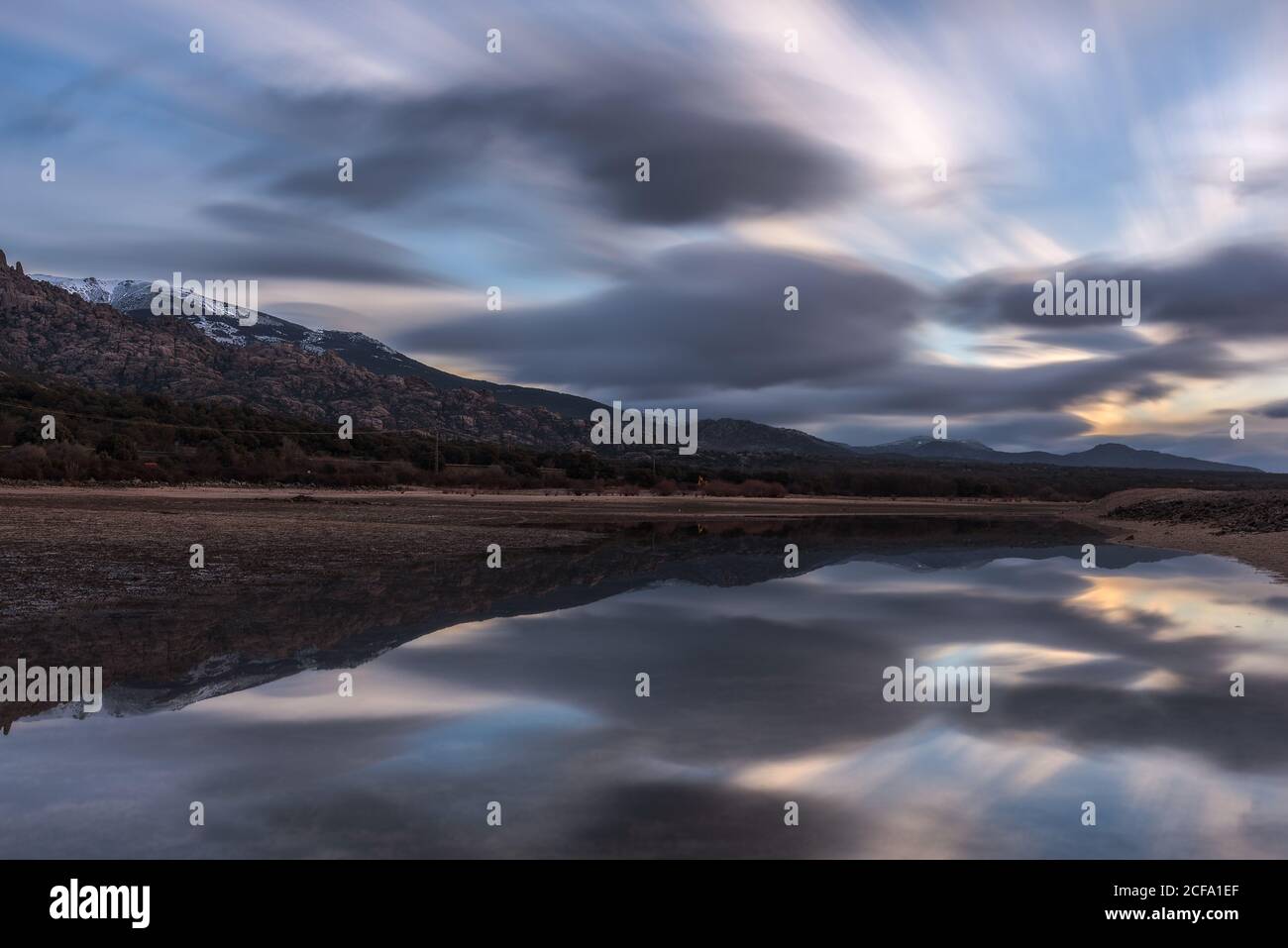 Long exposure picturesque view of cloudy sundown sky over mountain and peaceful lake water in nature Stock Photo