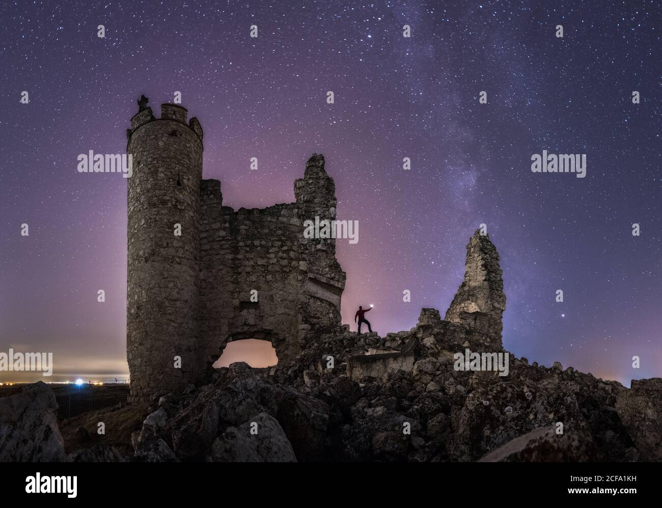 From below back view of anonymous tourist with lantern exploring ruined old castle under Milky Way at starry night Stock Photo