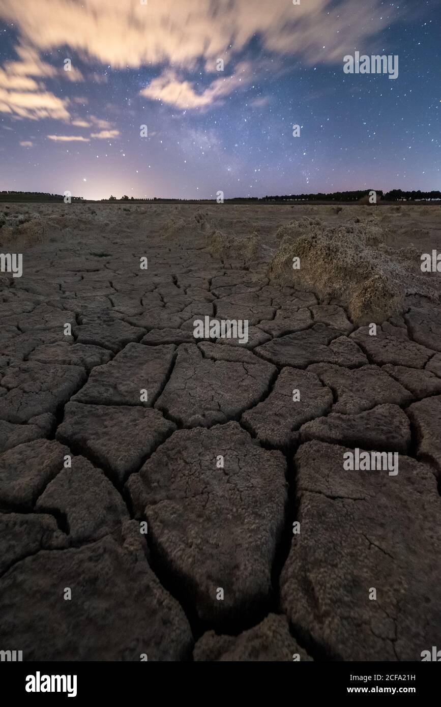 Drought cracked lifeless ground under colorful cloudy sky at sunset time Stock Photo