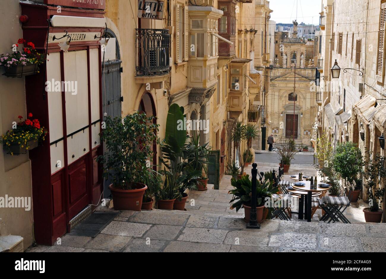 The historic Church of St. Lucy sits at the foot of a pedestrian section of St. Lucia Street lined with shops and restaurants in Valletta, Malta. Stock Photo