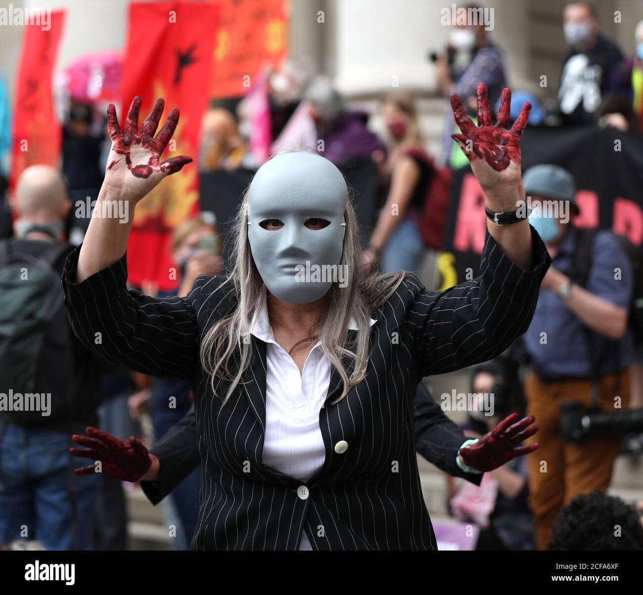 A masked protester, hands covered with fake blood, stands outside the ...
