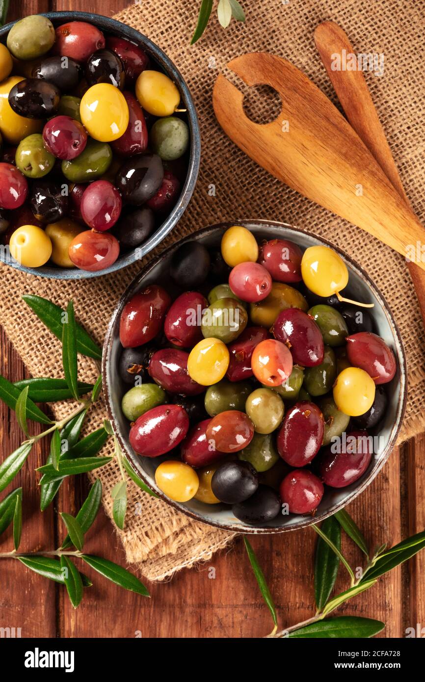 Olives. A variety of green, black and red olives, with leaves on a rustic wooden background, shot from the top Stock Photo