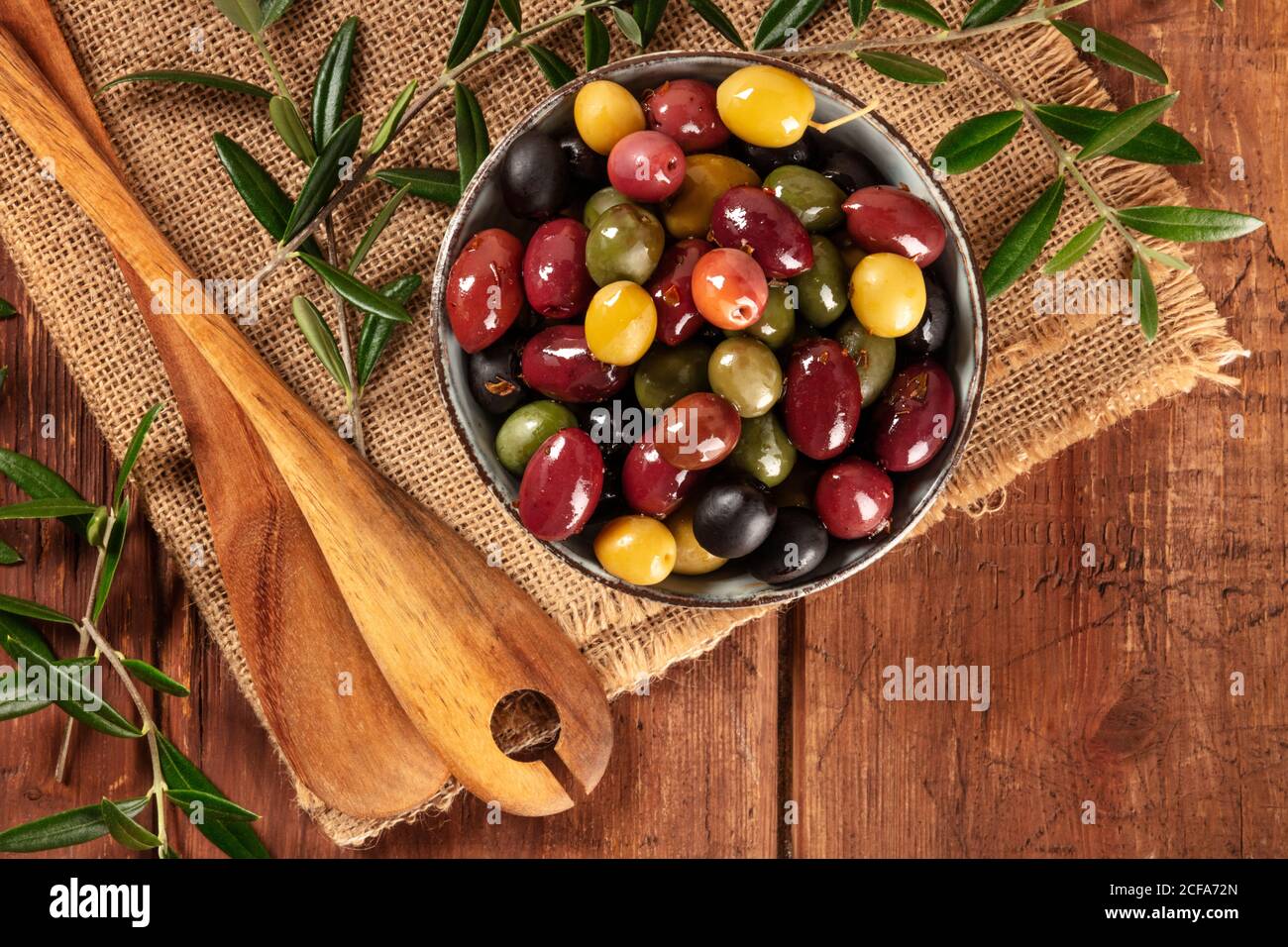 Olives. A variety of green, black and red olives, with leaves, shot from above on a rustic wooden background with a place for text Stock Photo