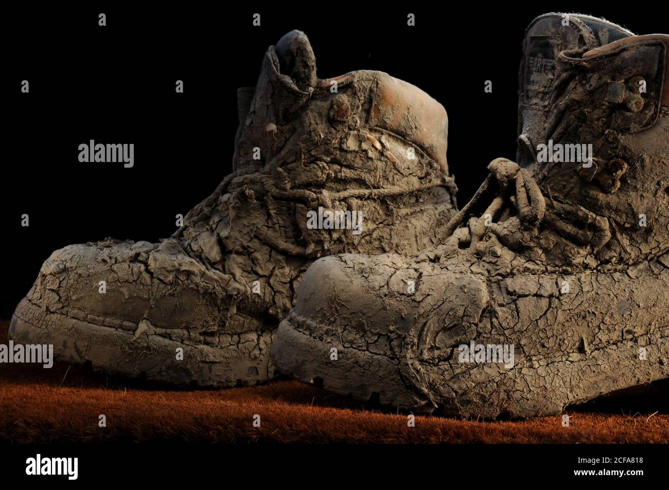 Pair of old worn walking boots covered in dried on thick mud with